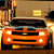 Pixelated orange car with black grille and headlights, positioned in front of a building with yellow windows and a striped pole.