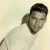 Pixelated static image of a person with dark hair and light skin wearing a white shirt against a pale background.