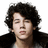 Pixelated close-up of a person with dark curly hair, closed eyes, and light skin wearing a black jacket over a white shirt against a plain background.