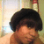 Pixelated close-up of a person with dark curly hair and light skin, wearing brown clothing against a blurred background.