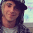 Pixelated portrait of a person with long dark hair wearing a dark cap and light-colored top against a pale background.