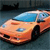 Pixelated image of a light orange sports car with a blue roof, viewed from a low angle against a dark background.