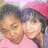 Two people in pink clothing and a red hat pose closely together, with one person's head positioned near the other's shoulder