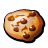 Pixelated circular icon with brown and tan tones showing a cookie-like object featuring scattered chocolate chips on its surface.