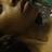 A pixelated close-up of a figure with brown hair and dark clothing against a light background, showing partial facial features and a blurred environment.
