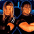 Pixelated static image of two orange-brown figures with long hair against a dark background, featuring blue structural elements and heart shapes.