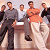 Pixelated static image of a group of men standing together in various poses and clothing styles against a light background.