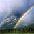 A static pixelated image shows a diagonal rainbow arc spanning from lower-left to upper-right against a blurred sky and landscape background.