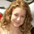Pixelated close-up of a person with light brown curly hair, closed eyes, and a slight smile against a blurred background.
