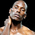 Pixelated image of a shirtless person with light skin tone, bald head, and hand near neck against black background.