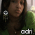 A pixelated image shows a person with long dark hair wearing a dark top, with green foliage and a light background, and the text 'adri.' in white pixelated letters at the bottom right.