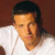 Static pixelated image of a person with dark hair wearing a white shirt against a brown background.