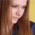Pixelated close-up of a person with long brown hair wearing a dark blue top against a yellow background.