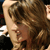 Pixelated close-up of a person with light brown hair and a neutral expression, cropped to show only the upper face and hair against a dark background.