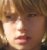 Pixelated close-up of a person's face with light brown hair, visible eyes, nose, and mouth against a blurred background.