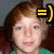 A pixelated close-up of a person with brown hair and a green top, featuring a black and yellow graphic symbol on the right side.