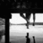 Black-and-white pixelated image of a figure standing on a platform beneath a structure with hanging elements, viewed from a low angle.