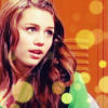 A static image of a person with long wavy brown hair wearing a green garment against an orange background with yellow circular bokeh effects.
