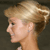 Pixelated profile view of a person with light brown hair styled in an updo, wearing a small earring, against a dark background.