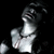 Pixelated grayscale image of a person with dark hair, wearing a light-colored top and dark necklace against black background.