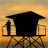 Silhouette of a person standing on a platform with a large dark structure against an orange-yellow gradient background.