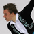 Pixelated static image of a person in profile wearing a white shirt and dark jacket with patterned sleeves, viewed from the side against a light gray background.