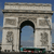 Static pixel art of a stone archway with an arched opening, flanked by decorative panels and a blue sky background.