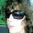 Pixelated portrait of a person with curly brown hair and dark sunglasses, surrounded by blue text on a light background.