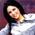 A pixelated figure with long dark hair wears a white top against a blurred purple and red background.