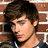 A pixelated image shows a person with brown hair against a brick wall, next to bright blue background with pink text.