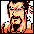 Pixelated static image of a man with long hair and glasses in orange/yellow tones against gray background, wearing white shoulder accents.