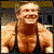 A static image of a person with short light brown hair wearing a dark sleeveless top, smiling broadly against a blurred background.