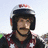 Pixelated image of a person wearing a dark helmet with red and white accents, a dark jacket with red and white details, and a black chin strap.