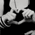 Black-and-white image of hands forming a heart shape with fingers, one hand holding a small object near the center.