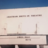 Static image of a building facade with horizontal lines and vertical elements under a blue sky.