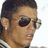 Pixelated close-up of a person with short dark hair wearing large black sunglasses and a light-colored checkered shirt, cropped to show only the head and shoulders against a white background.