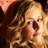 Pixelated close-up of a person with light brown hair and a neutral expression, set against a dark background with warm tones.