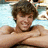 Pixelated image of a person with brown curly hair, light skin tone, and visible facial features including eyes, nose, mouth, and beard stubble.
