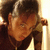 Pixelated close-up of a person with dark hair and brown skin, wearing a dark top against a light background.