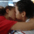 Two people in close embrace, one wearing red shirt and white tank top, with visible arm around the other's back.