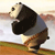 Pixelated panda in mid-stride wearing a dark blue shirt and brown pants on a blurred background with green and brown ground elements.