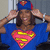 A person wearing a blue shirt with a red and yellow Superman logo, adjusting a blue cap with red trim.