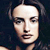 Pixelated close-up of a person's face with light skin tone, dark hair, and neutral expression against dark background.