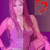 Pixelated image of a person with long pink hair wearing a sleeveless top, standing against a purple background with red circular shapes.