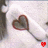 A pixelated heart-shaped object with a dark brown outline and gray interior, attached to a thin gray stem, with a small red pixelated heart at the stem's end against a light gray background.