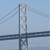 Pixelated static image of a suspension bridge with steel cables and a roadway against a light blue sky background.