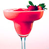 A red frozen drink in a stemmed glass with a strawberry and mint garnish on a light pink background.