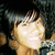 A person with dark hair and bangs smiles in a pixelated image, wearing a patterned garment against a dark background.