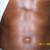 A pixelated close-up of a person's forehead and upper face with light skin tone, brown hair on the sides, and a small circular symbol near the bottom center.
