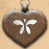 Brown heart-shaped pendant with white butterfly design and metal loop at top, set against light brown background.